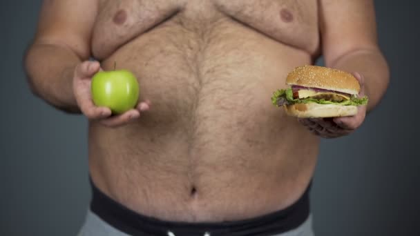 Fat man kiezen van apple in plaats van de hamburger, houden van gezonde voeding, buik closeup - Video