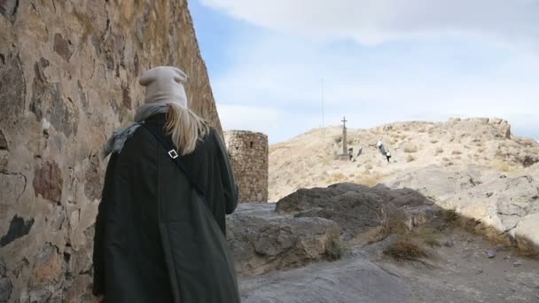 Молодая туристка в зеленой кожаной куртке идет вдоль крепостной стены древнего монастыря
 - Кадры, видео