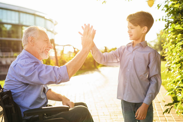 High five. The old man in a wheelchair greets his grandson - Photo, Image