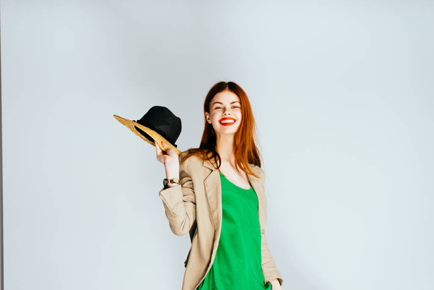 happy red-haired girl with red lipstick, in a green sweater holding a hat in her hand, smiling - Фото, изображение