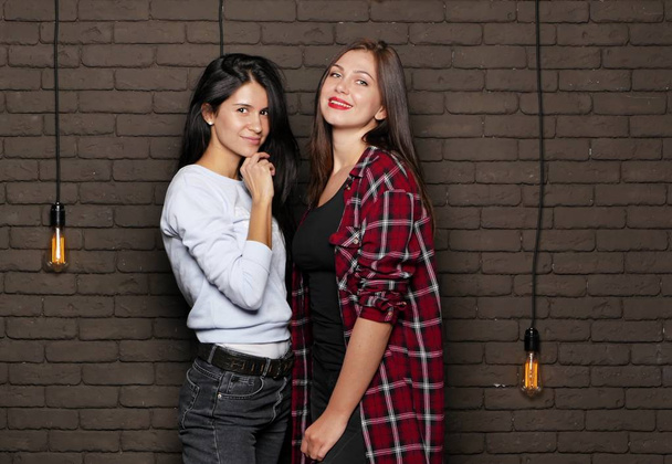 Two young and beautiful womans are posing near the brick wall - Photo, image