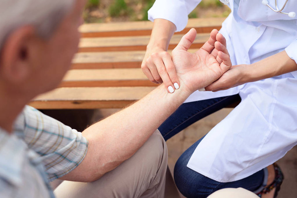 The doctor measure the patient's pulse while sitting on a bench in the park - Photo, image