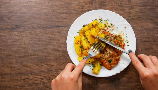 woman hand holding fork and knife with Grilled chicken breast with potato in a plate on a wooden background. with copy space. top view - Foto, Imagen