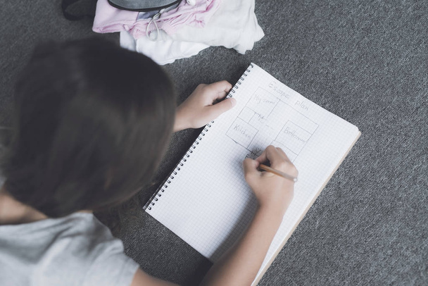 Dark-haired girl lies on the floor and draws a pencil in white notebook with a pencil plan - Photo, image
