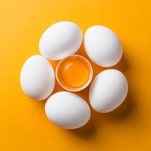 White eggs and egg yolk on the yellow background. topview, square - Фото, изображение