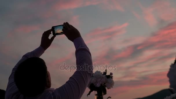 El hombre al atardecer toma fotos del cielo colorido en el teléfono
. - Metraje, vídeo