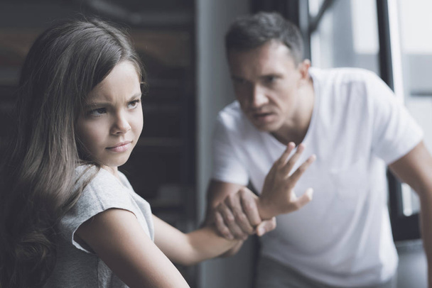The spiteful father grabbed his daughter's hand, which turns away with disgust from him - Фото, изображение