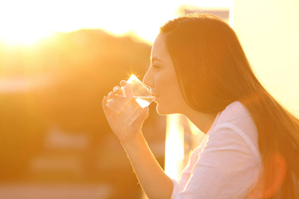 Woman drinking water from a glass at sunset - Foto, afbeelding