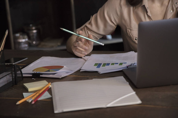 Business woman holding pencil and working on laptop at table with documents - Photo, image