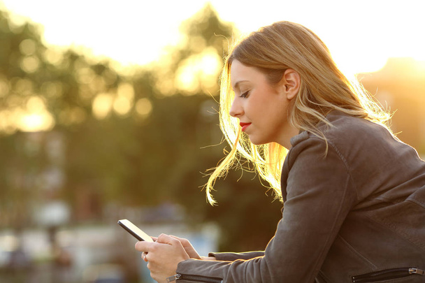 Mujer leyendo texto en un teléfono inteligente al atardecer
 - Foto, imagen
