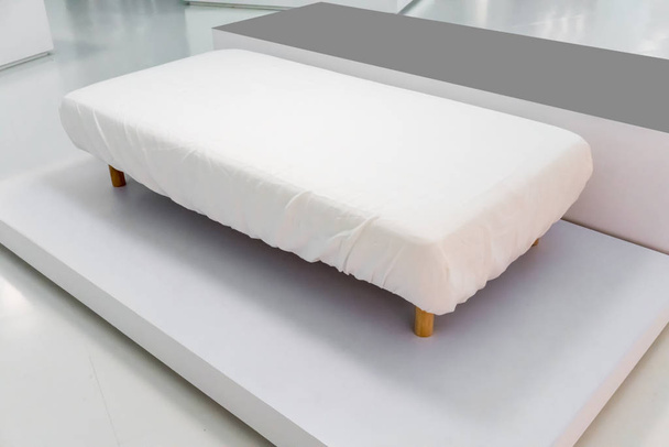 Gloednieuwe slaapbank met witte cover uitgerust blad en houten been  - Foto, afbeelding