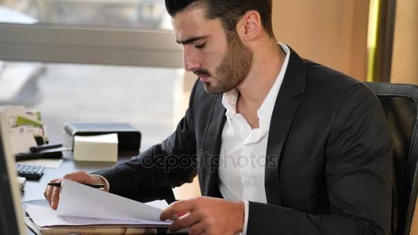 Handsome young businessman sitting at desk in office - Filmati, video