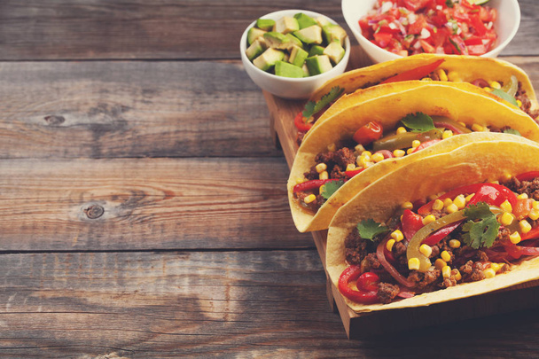 Kolme meksikolaista tacoa jauhelihalla ja sekoita vihanneksia vanhalla maalaispöydällä. Meksikolainen ruokalaji kastikkeilla salsaa kulhossa ja avokado. Mausteista ja kuumaa katuruokaa. kopiotilaa
 - Valokuva, kuva
