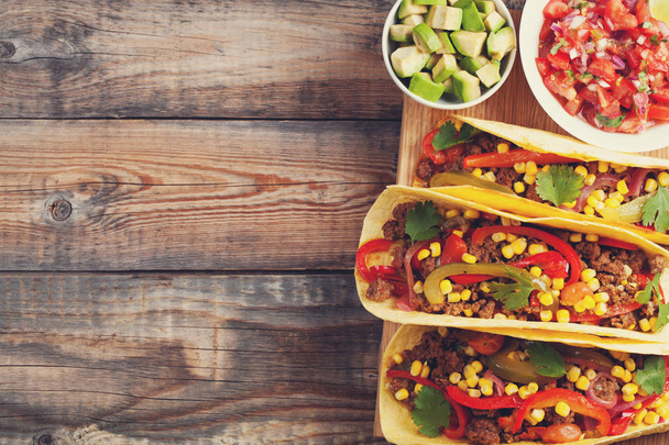 Kolme meksikolaista tacoa jauhelihalla ja sekoita vihanneksia vanhalla maalaispöydällä. Meksikolainen ruokalaji kastikkeilla salsaa kulhossa ja avokado. Mausteista ja kuumaa katuruokaa. Top näkymä kopioi tilaa
 - Valokuva, kuva