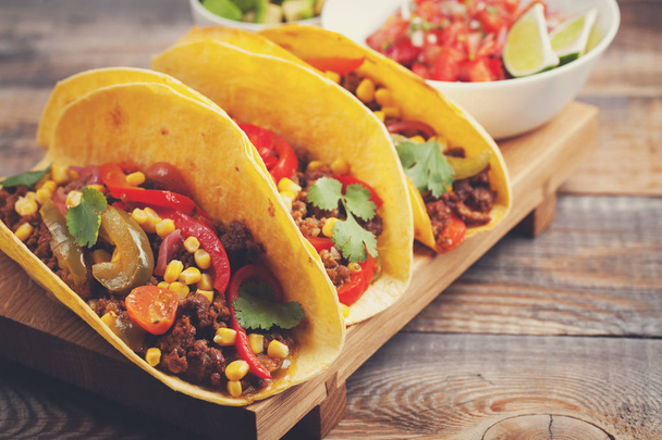 Trzy meksykańskie tacos z mielonego mięsa wołowego i mix warzyw na starej tabeli stylu rustykalnym. Meksykańskie danie z sosem salsa w misce i awokado. Gorące i pikantne żywności ulicy. Szczelnie-do góry - Zdjęcie, obraz