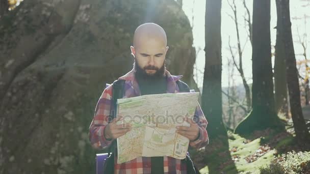 Stylish hipster man traveler with backpack holding map and exploring on top of mountains, travel concept - Video