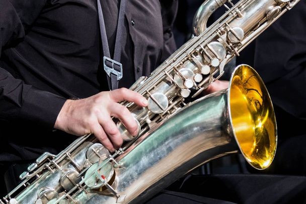 A mão direita do músico em uma camisa preta apoia-se em um saxofone-barítono. Close-up
. - Foto, Imagem