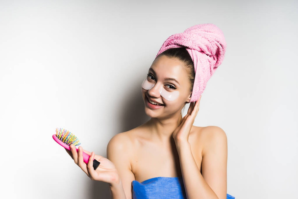 young beautiful girl smiling, wearing a pink towel, holding a hairbrush in her hand - Fotó, kép