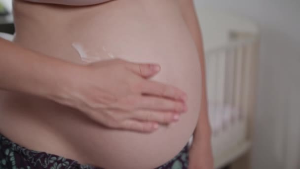 Nuori raskaana oleva nainen hieroo kermaa vatsaansa
 - Materiaali, video
