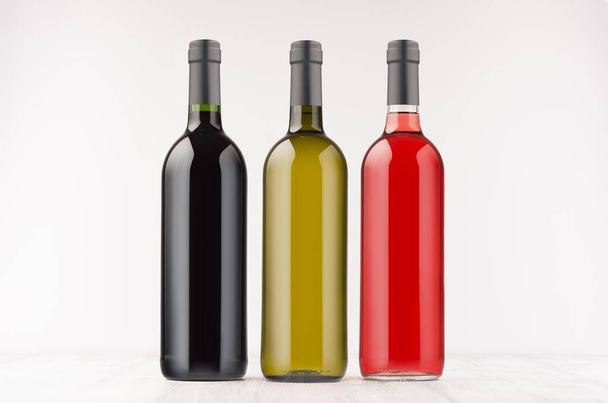 Three wine bottles  different colors  on white wooden board, mock up.  - Фото, изображение