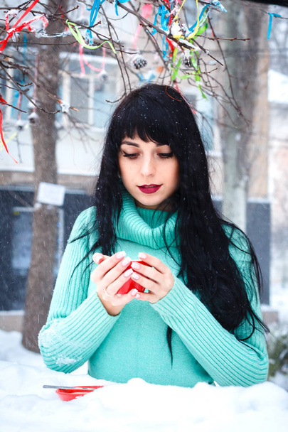 Beautiful young woman drinks a coffe in street cafe at snowy win - Photo, Image