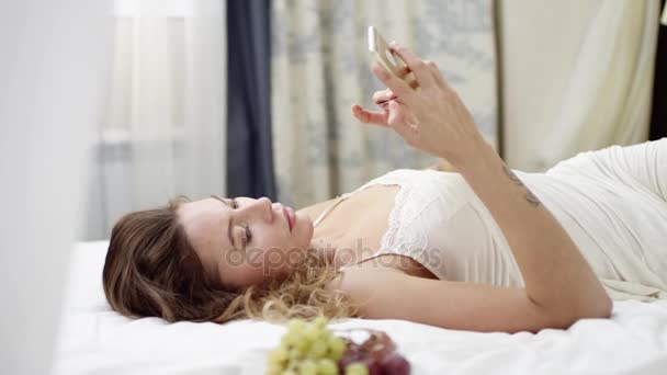 Žena nakupování on-line pomocí kreditní karty a smartphone vleže na posteli - Záběry, video