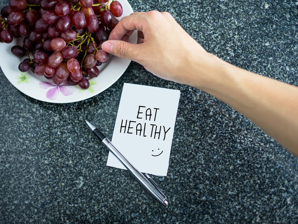 Eat Healthy text on paper note with hand picking grape - Photo, Image