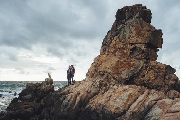 Young couple of travelers at rocky seacoast - 写真・画像