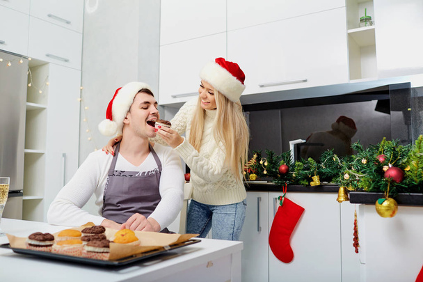 A couple in Santa Claus hats bake cupcakes on Christmas in the k - Fotografie, Obrázek