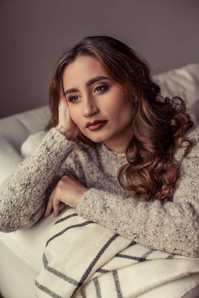 Een gezellige portret van een jonge mooie vrouw. Mooie Turks meisje. Warme herfst. Gezellig huis avond. Een jonge vrouw zichzelf gewikkeld in een deken en zit op de Bank. - Foto, afbeelding