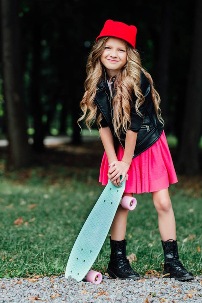 Portrait stylish fashion little girl child posing with skateboard on city park. - Zdjęcie, obraz