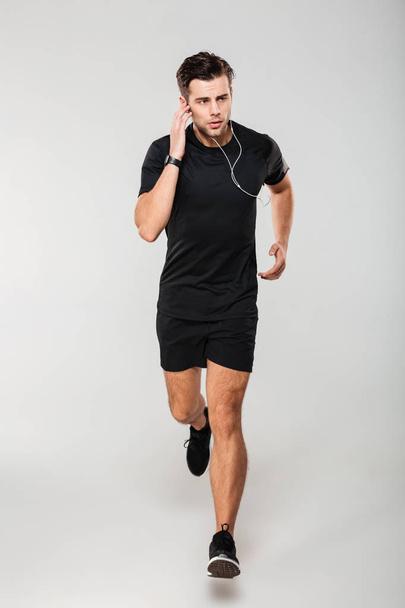 Full length portrait of a young man athlete in earphones - Photo, Image