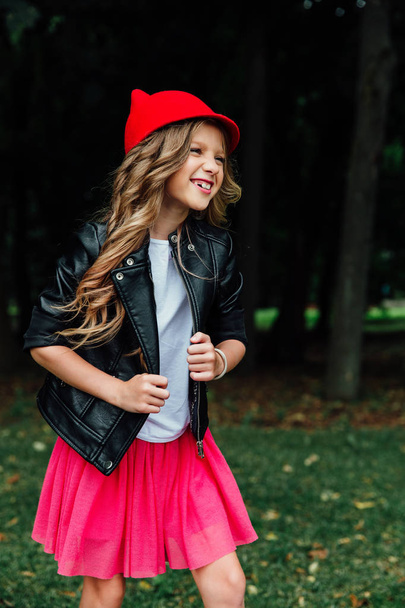 Outdoor lifestyle portrait of stylish little girl teenager on city park. . Beautiful child, wearing. - Фото, изображение