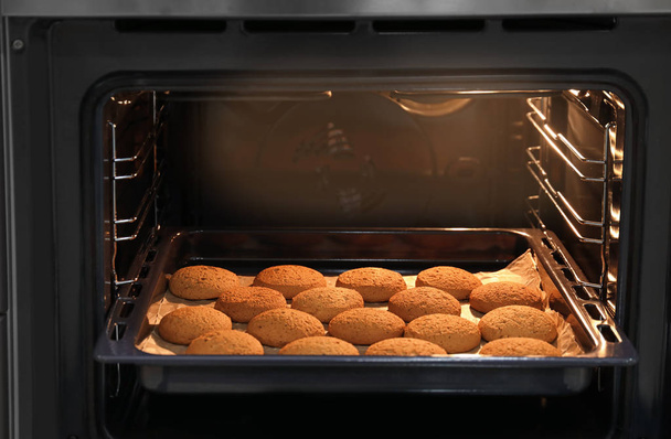 Baking tray with delicious oatmeal cookies in oven - Фото, зображення