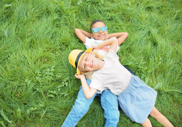Милые модные дети лежат на зеленой лужайке под открытым небом
 - Фото, изображение