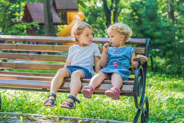 Toddlers boy and girl sitting on a bench by the sea and eat bread sticks. - Φωτογραφία, εικόνα