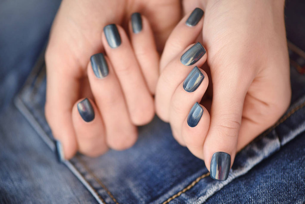 Manos con uñas manicura azul oscuro sobre fondo textil jeans
 - Foto, imagen