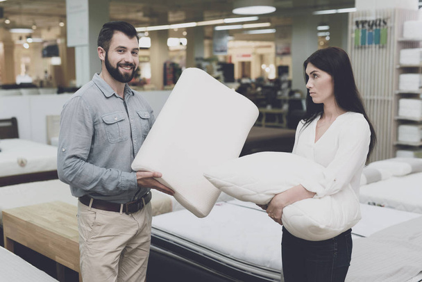 A couple in a large store of beds and mattresses chooses pillows. They examine several variants of pillows - Foto, Bild