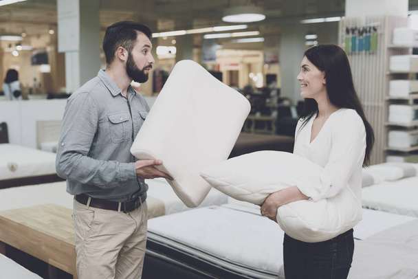 A couple in a large store of beds and mattresses chooses pillows. They examine several variants of pillows - Фото, изображение