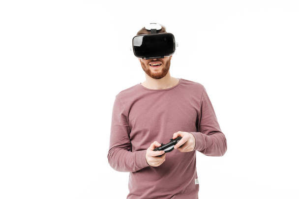 Молодой улыбающийся мужчина в очках виртуальной реальности и играет в видеоигры на белом фоне. Веселый мальчик с джойстиком в руках носит очки визуальной реальности изолированы
 - Фото, изображение