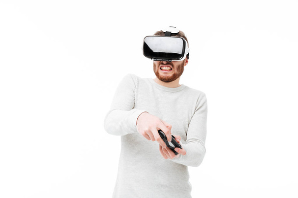Portret van een jonge man met behulp van virtual reality bril en afspelen van video game op witte achtergrond. Jongen met joystick in handen visuele werkelijkheid bril geïsoleerd - Foto, afbeelding