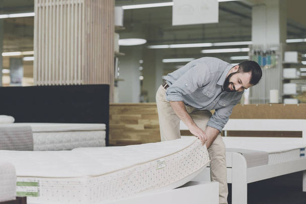 A man inspects a mattress in a mattress store. He lifted one of them - Zdjęcie, obraz
