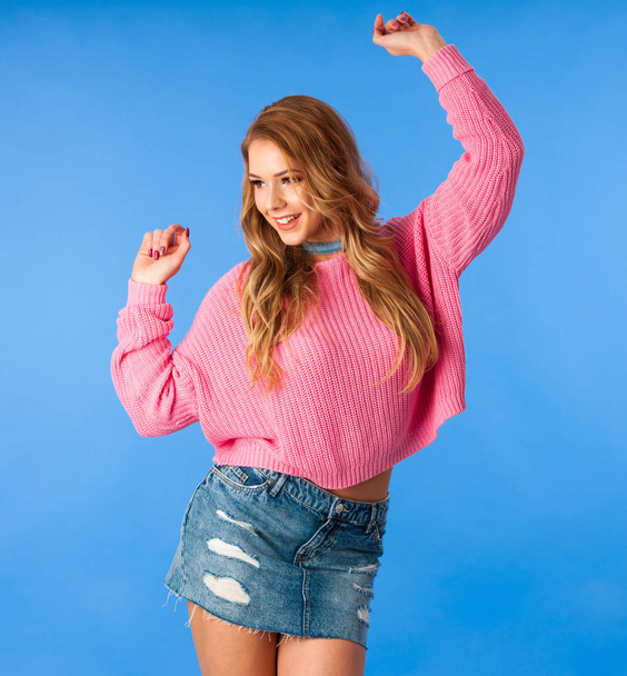 Beautiful young woman in pink sweater and jeans skirt over blue background - Valokuva, kuva
