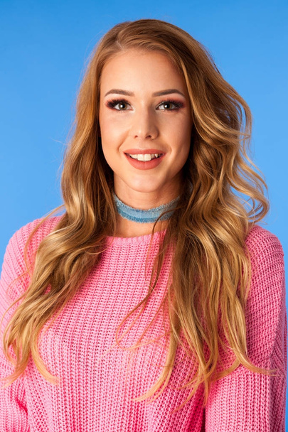 Beautiful young woman in pink sweater and jeans skirt over blue background - Photo, image