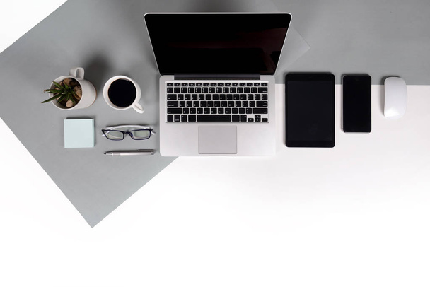 Flat lay photo of Office table with laptop computer, notebook, digital tablet, mobile phone, Pencil, eyeglasses  on modern two tone (white and grey) background. Desktop office mockup concept. - Foto, Imagen