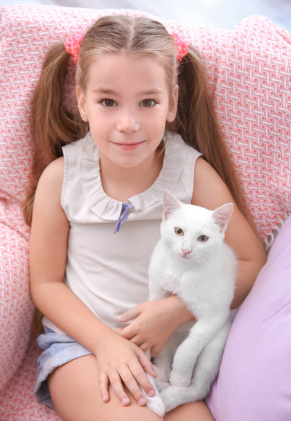 Little girl sitting in armchair with white cat indoors - Fotó, kép