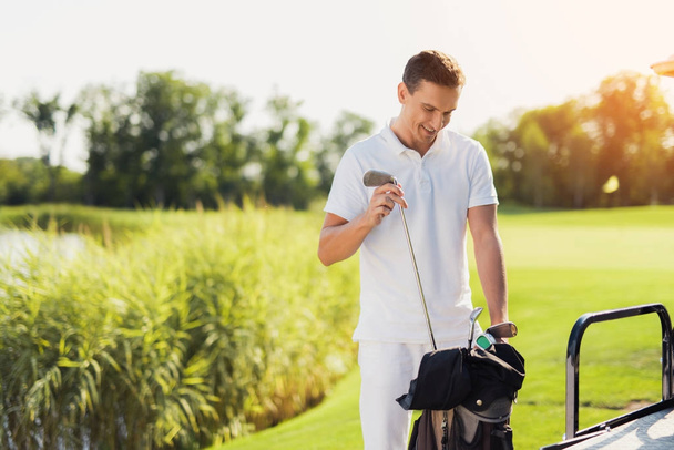 Egy férfi, fehér ruhát golf autó mögött áll, és kiválaszt egy bottal, a játék a zsákból - Fotó, kép