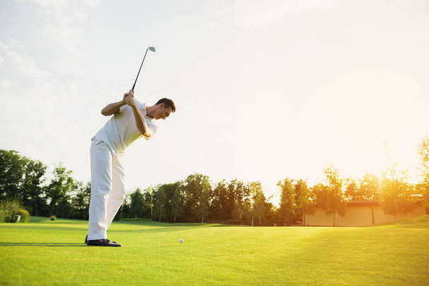 A man in a white suit plays golf. He took the stick and was preparing to strike - Фото, изображение