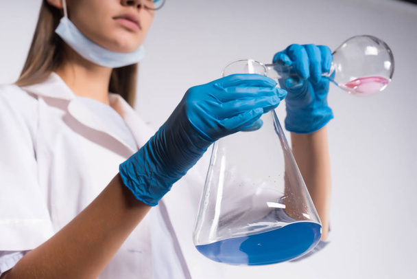 girl chemist in white medical gown and gloves holds flasks with chemicals - Φωτογραφία, εικόνα