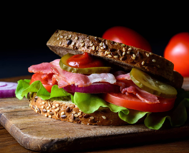 Sandwich freshly prepared with bacon, tomato, cucumber, onion on whole grain wheat toast - Foto, Imagem